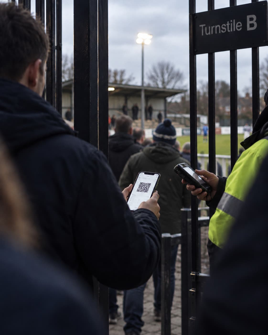 A fan showing the QR ticket on their phone to a steward with a scanner at the turnstile of a small football ground